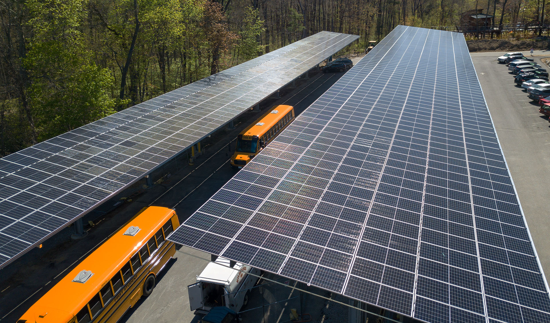 School busses parked under two large solar arrays in a park-and-ride lot.